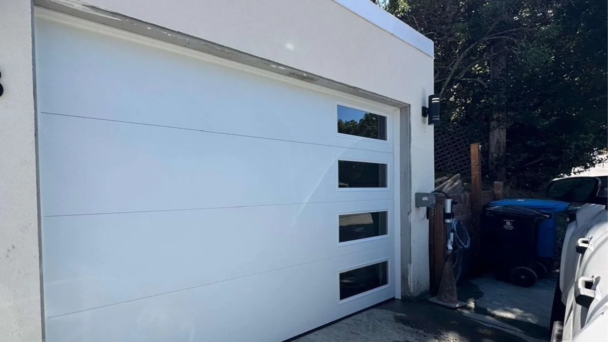 Modern white sectional garage door with a horizontal band of black-framed windows